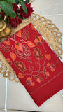Red ikkat saree with floral patterns on a decorative mat with roses and a lamp.